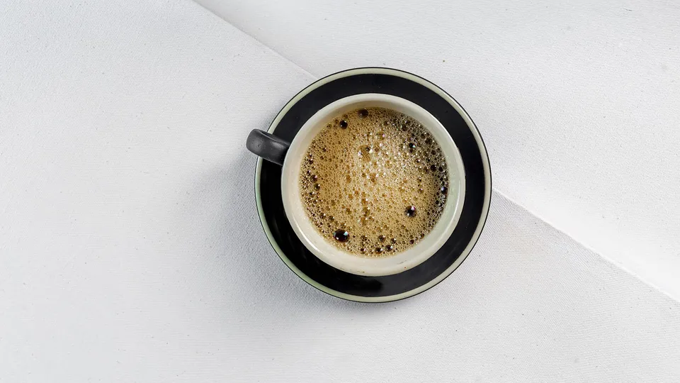 Espresso mit Crema in einer schwarzen Tasse auf heller Fläche, von oben fotografiert